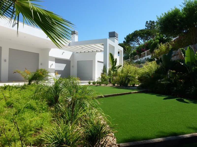 Modern private home with artificial grass and lush planting around it.