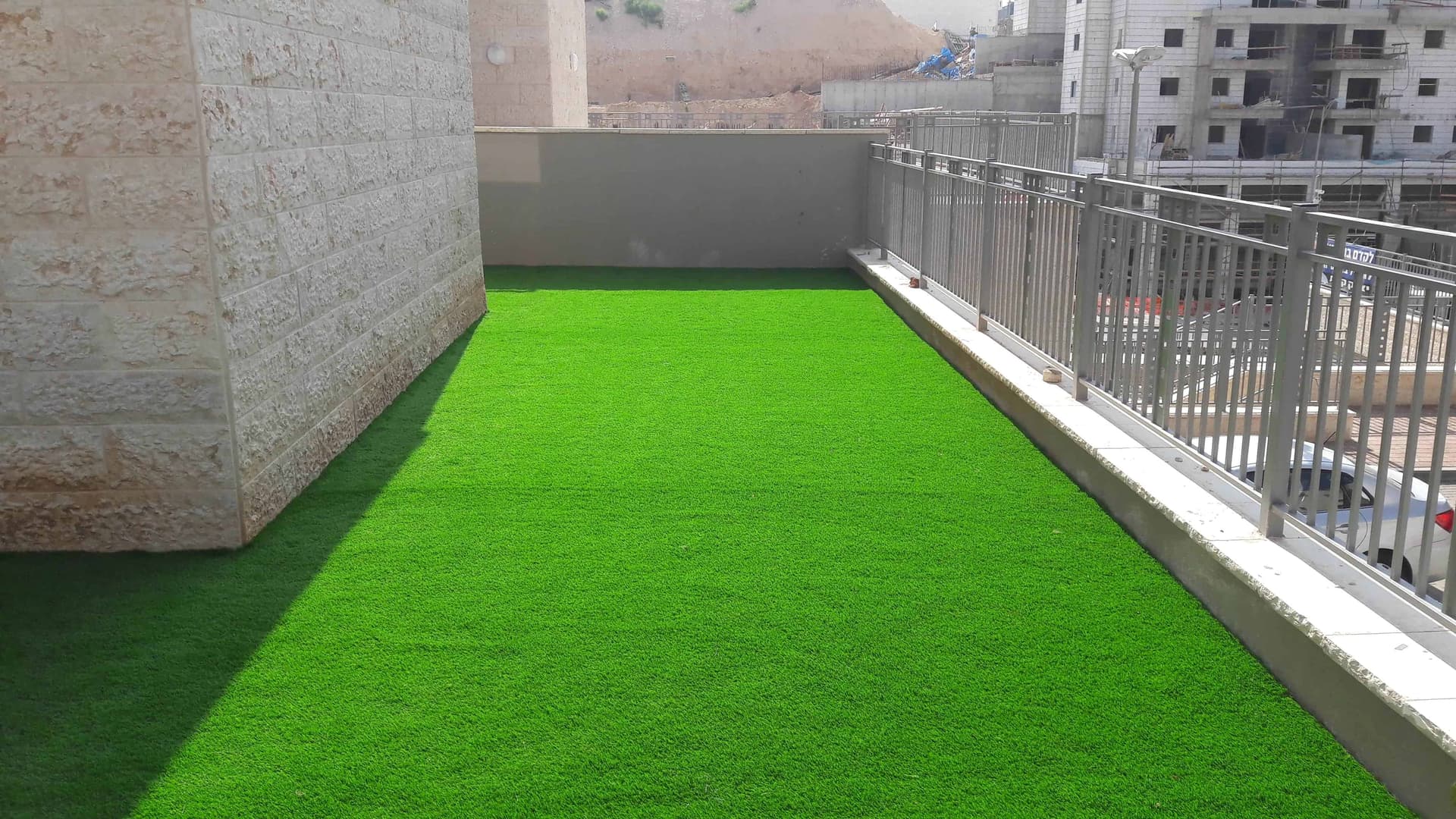 Grande terrasse urbaine avec gazon synthétique vert et garde-corps métallique.