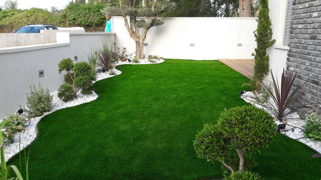 Private garden with artificial grass, a central tree, deck and white planting beds.