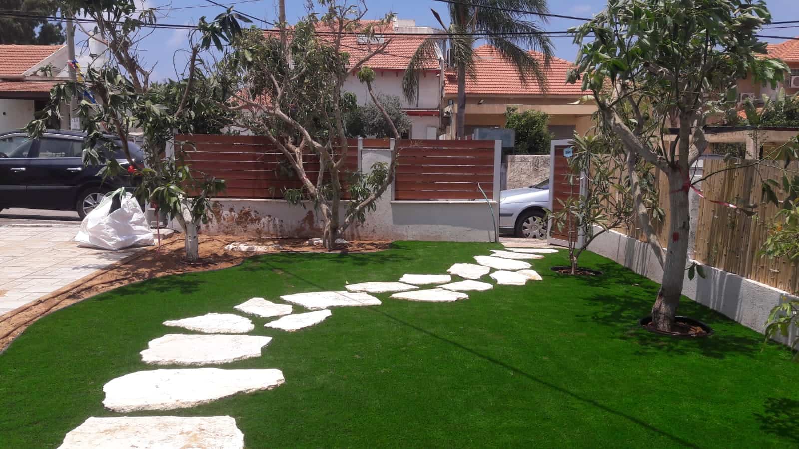 Front garden with green lawn, trees and white stepping stones.